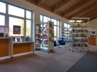 Blick in die Bücherei. Regale voll mit Büchern stehen vor einer blauen Sitzgruppe